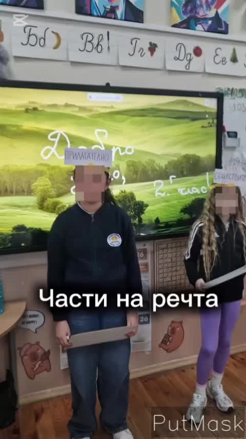Три деца стоят пред дъската, всяко с табела на челото за различна част на речта (прилагателно, съществително, глагол). Те държат малки бели дъски, на които пишат съответната дума, за да съставят заедно изречение.